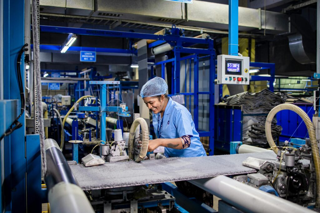 Indian female factory worker smiling while operating complex textile machinery in an industrial setting.